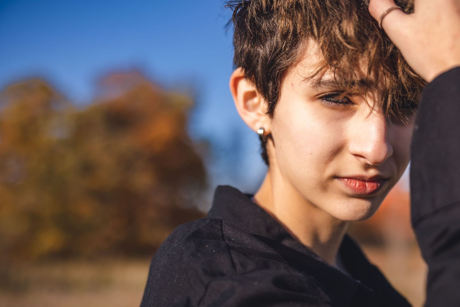 Close-up portrait in warm autumn sunlight against blurred fall foliage background.