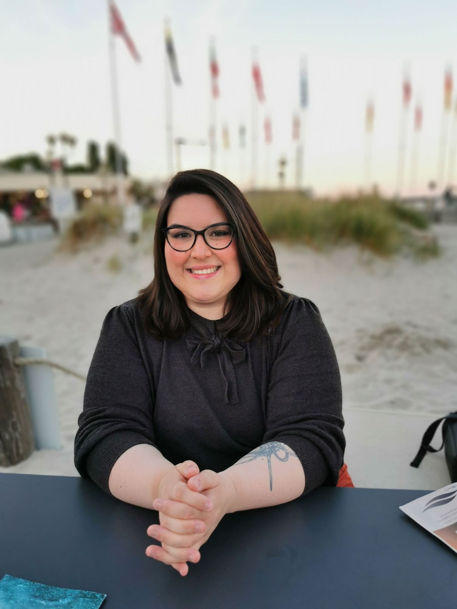 Casual outdoor portrait at beach with flags in background.