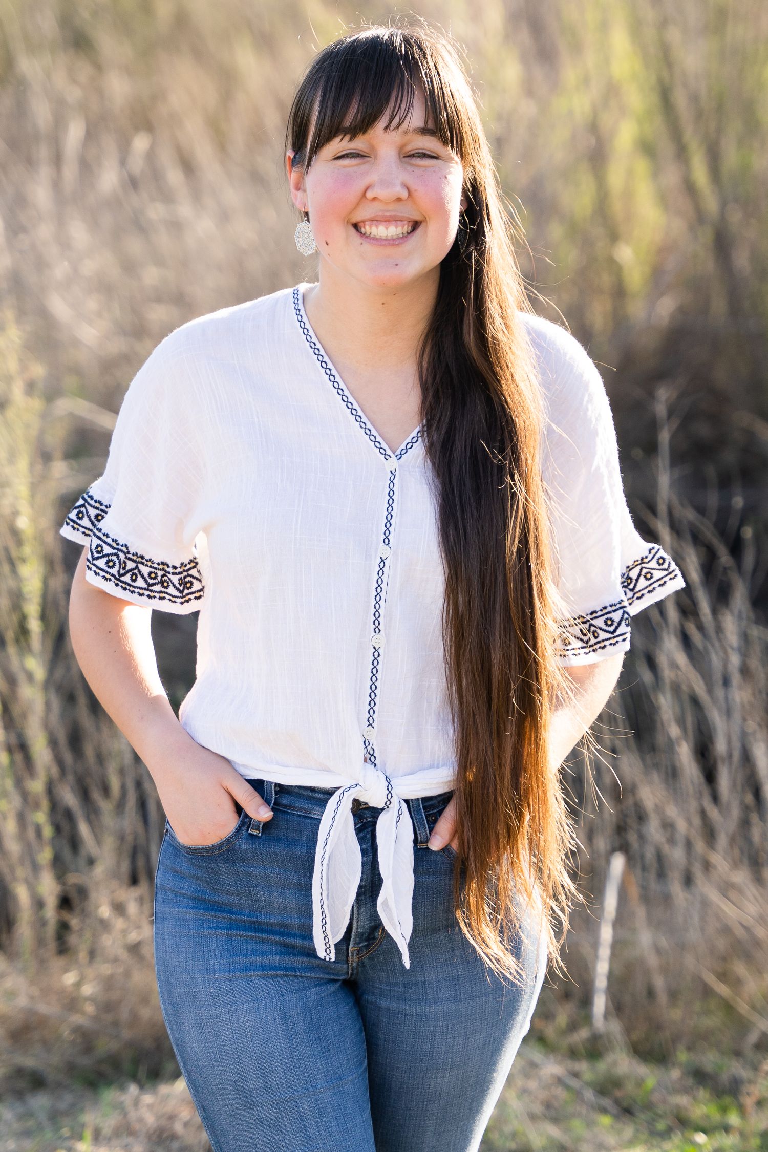 Girl with long brown hair wears jeans and smiles in a golden field.
