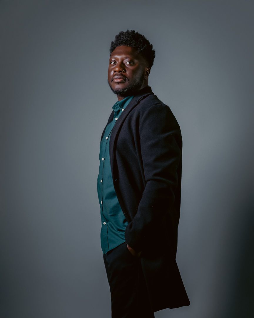 Professional studio portrait of man in dark blazer against grey background.
