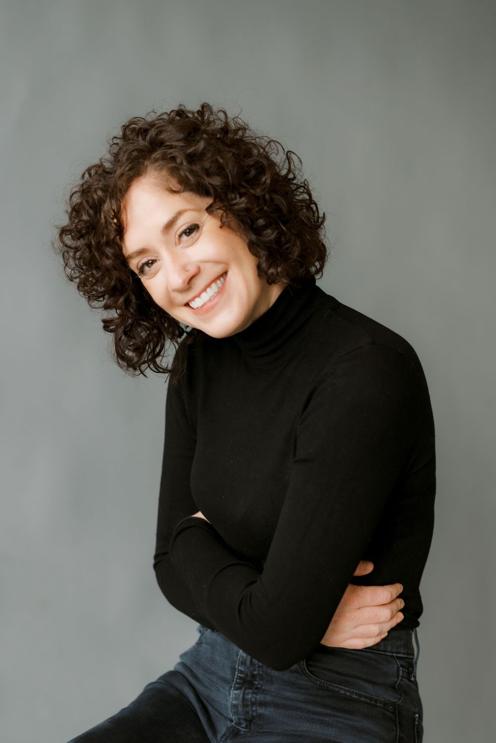 Casual portrait in black turtleneck with curly hair against minimal studio backdrop.