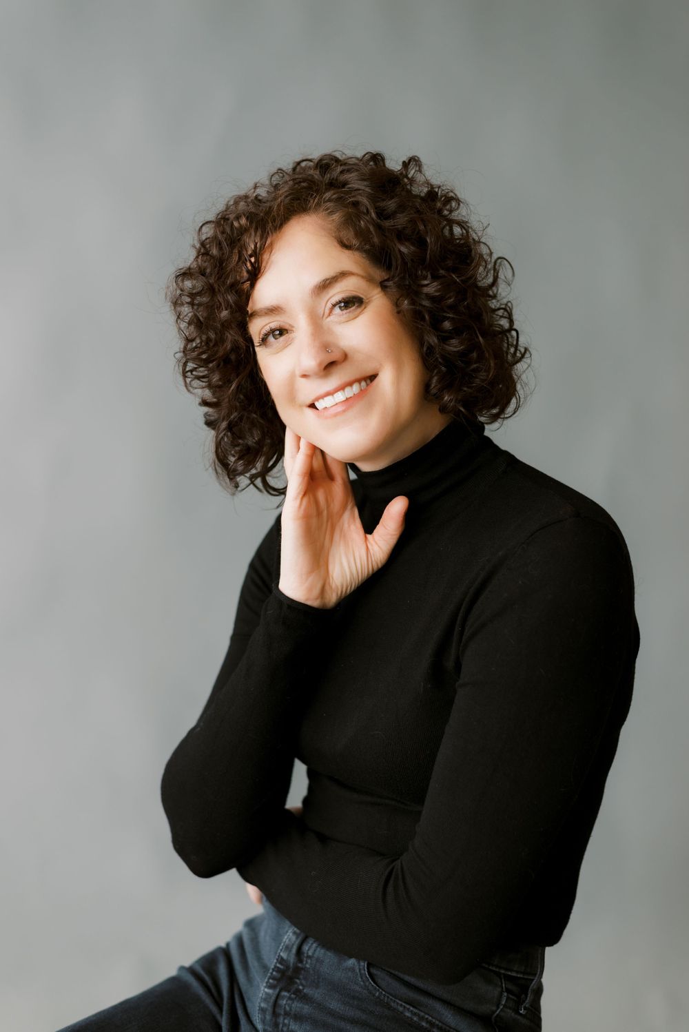 Professional portrait in black turtleneck against neutral gray background.