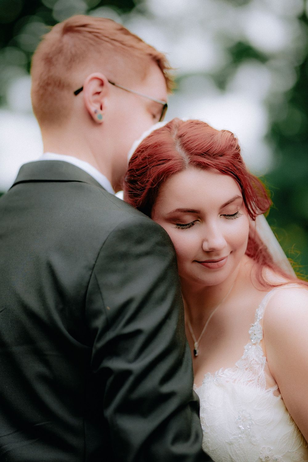 An intimate wedding portrait captured in soft focus with natural greenery in the background.