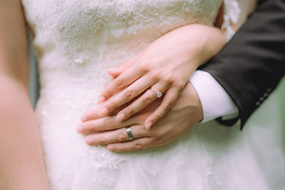 Close-up of newlywed hands showing wedding rings against a white lace dress.
