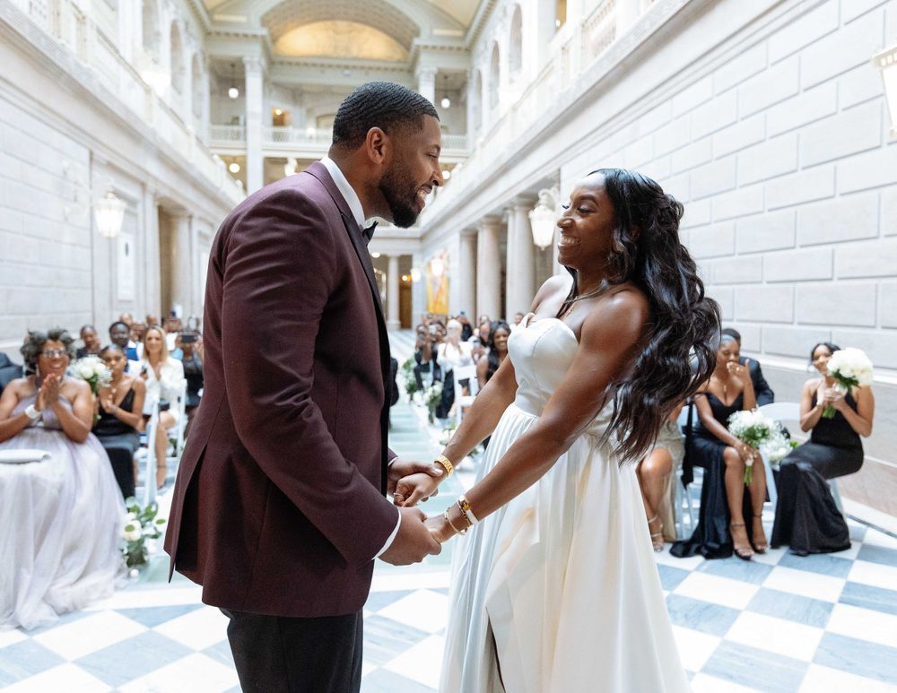 A joyful wedding celebration moment in an elegant white marble hallway with ornate architectural details.