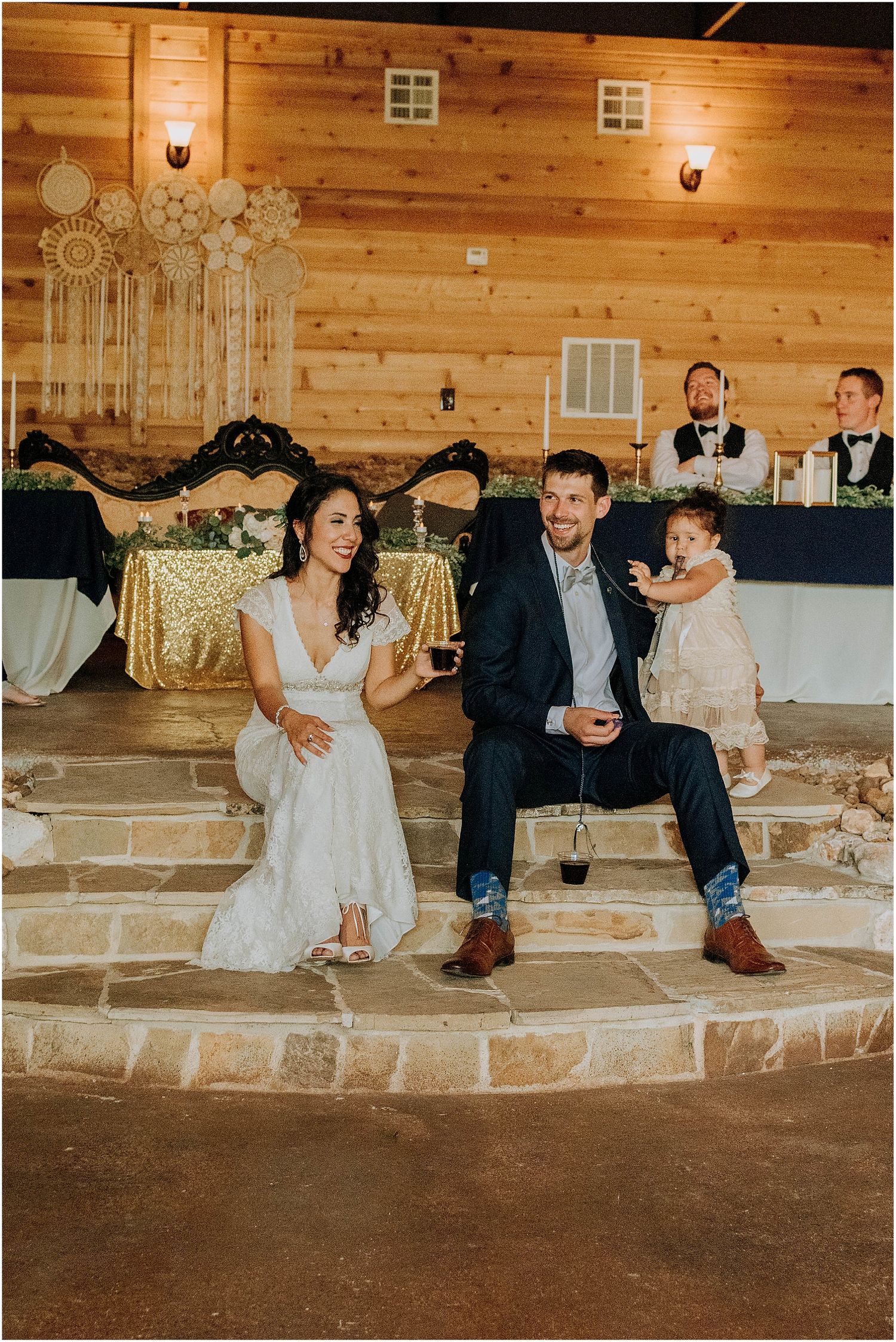 A wedding couple seated on stone steps in a rustic barn venue with decorative lighting and decor.