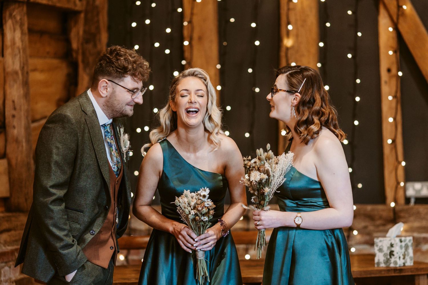Three wedding attendees share a candid moment under twinkling fairy lights.