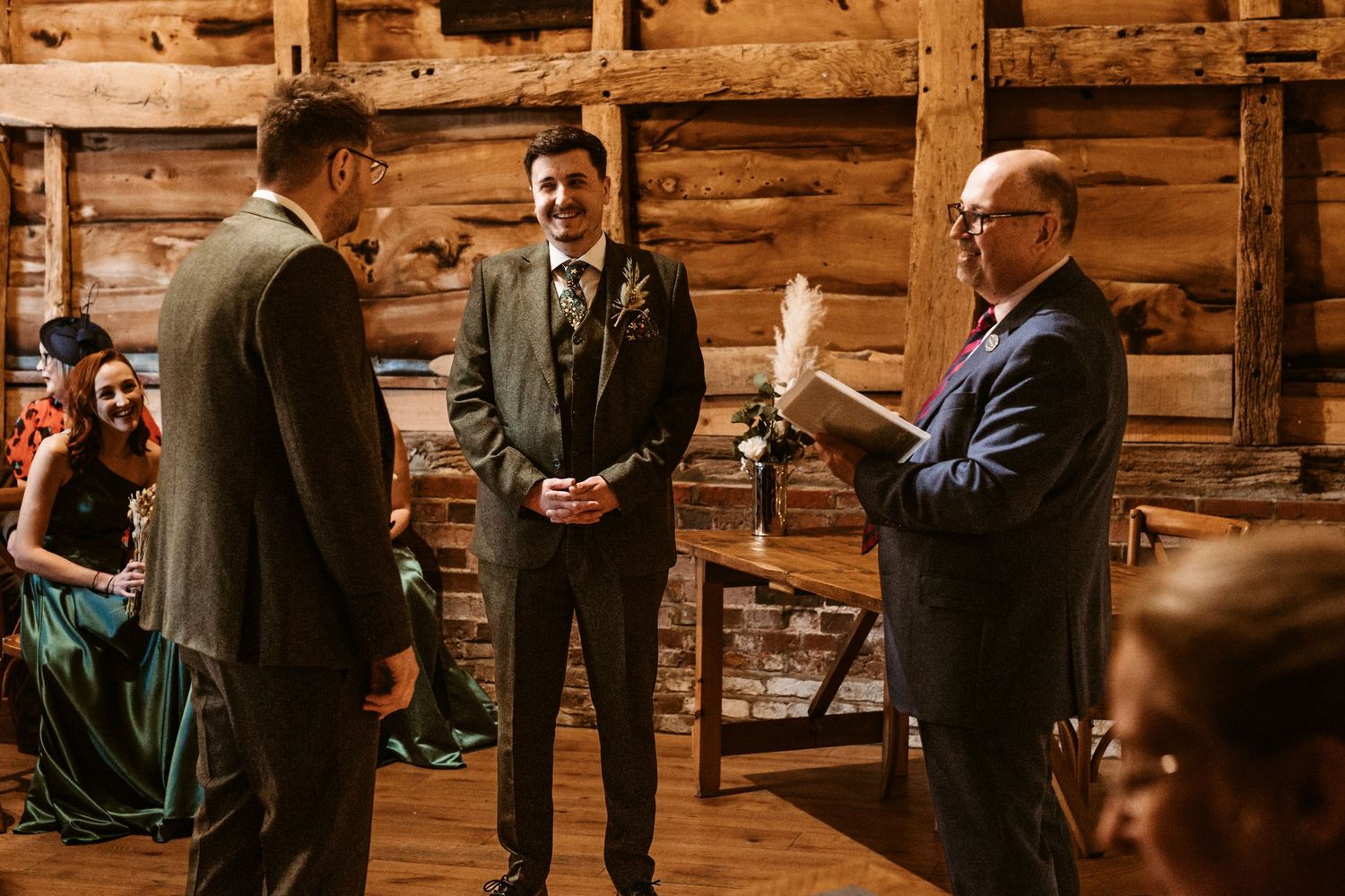 Wedding ceremony in a rustic barn with wooden walls and guests watching the exchange of vows.