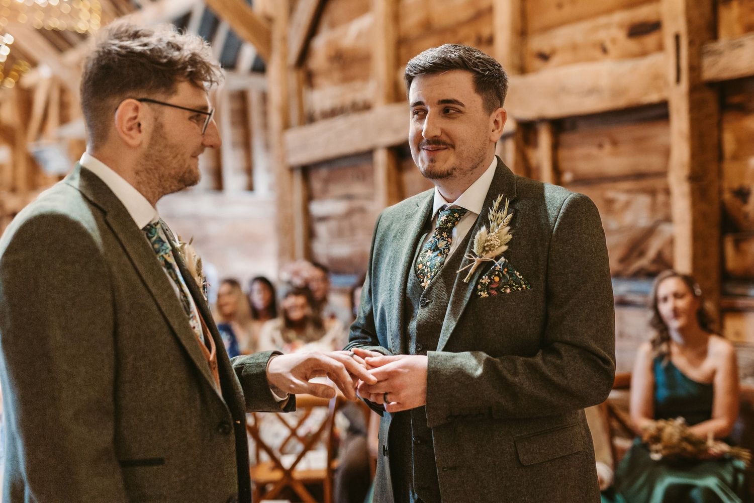Two people exchanging rings during an intimate rustic barn wedding ceremony with wooden beams and warm lighting.