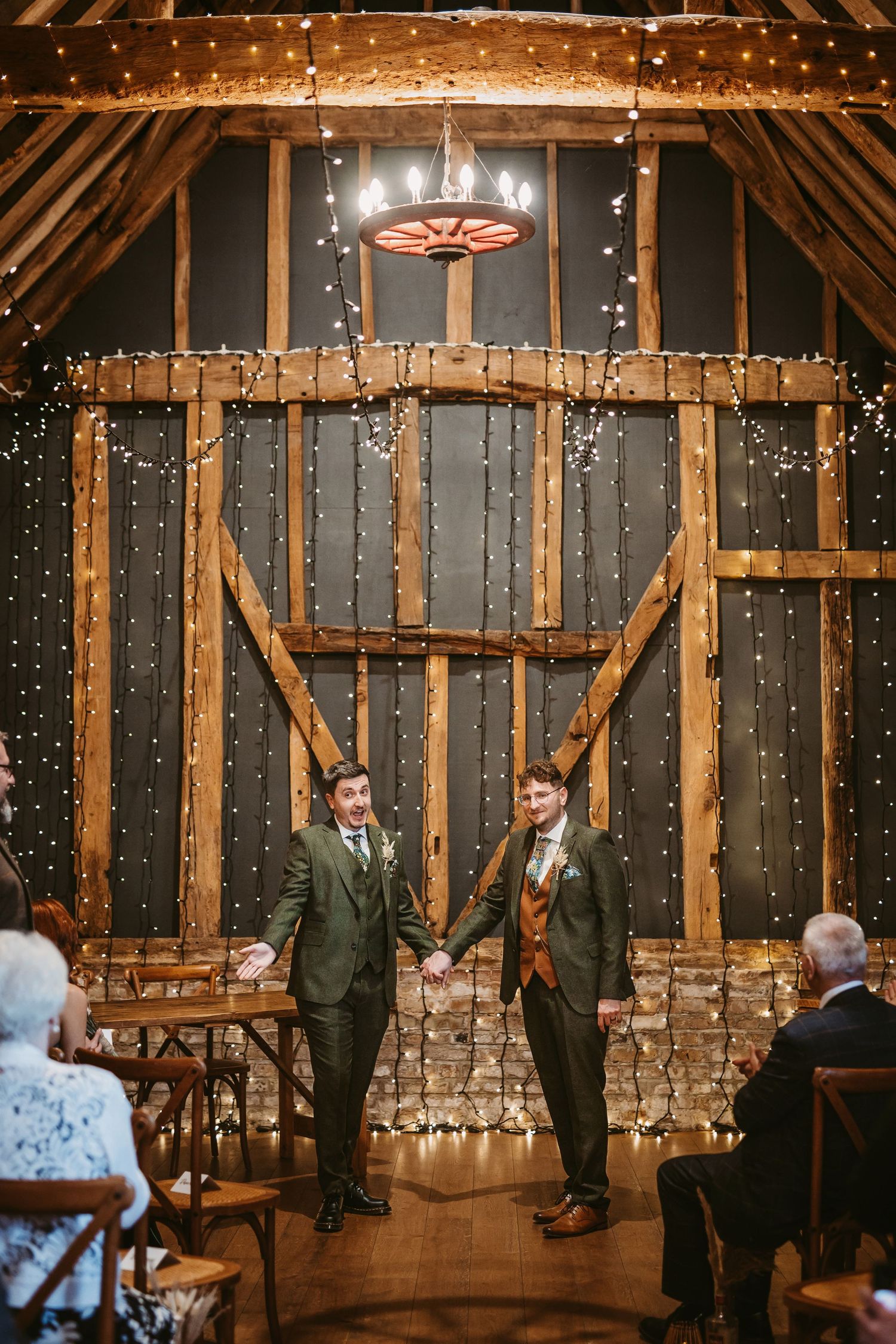 Couple standing under twinkling lights in rustic barn venue during wedding ceremony.