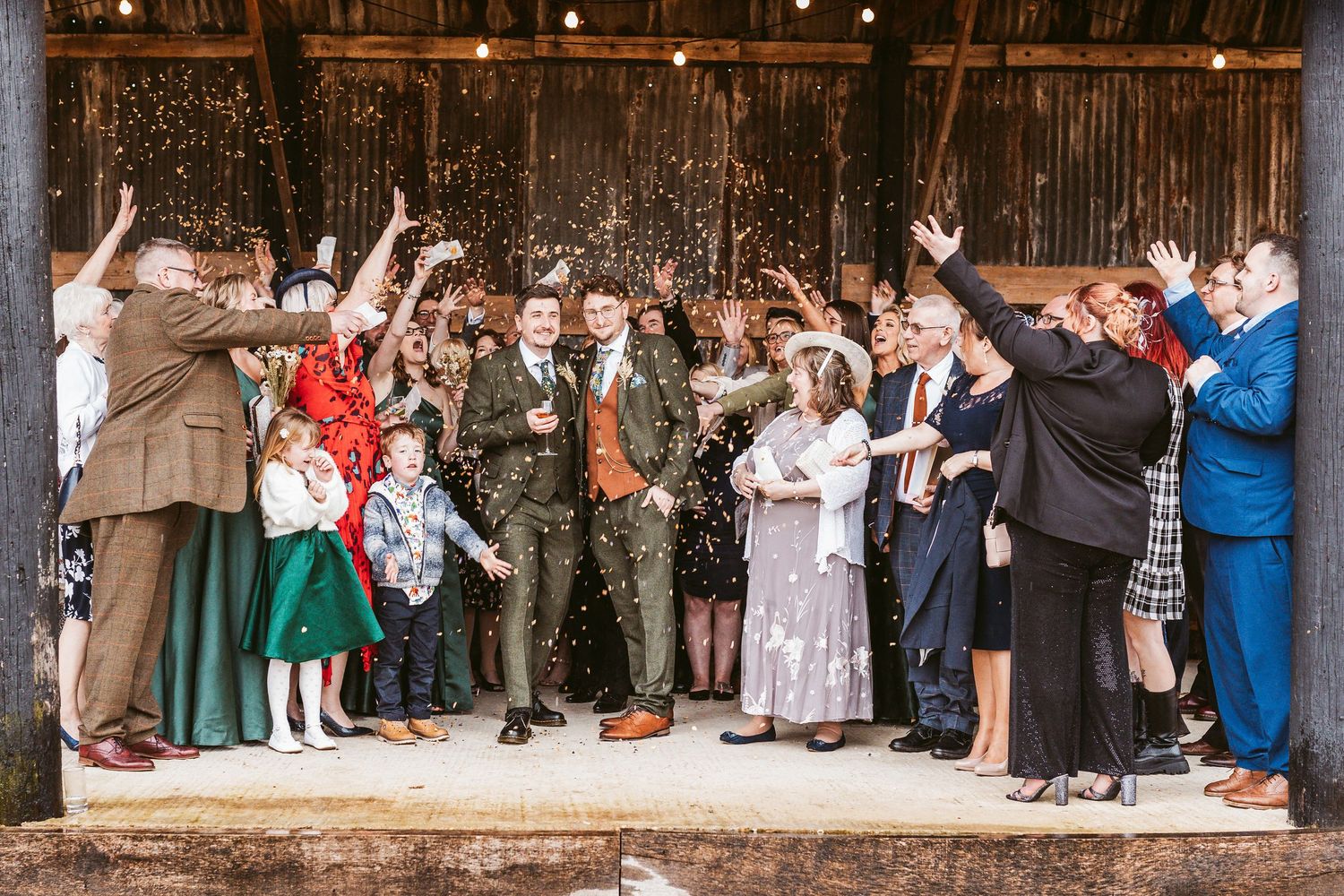 Wedding party celebrates with arms raised in front of rustic barn setting.