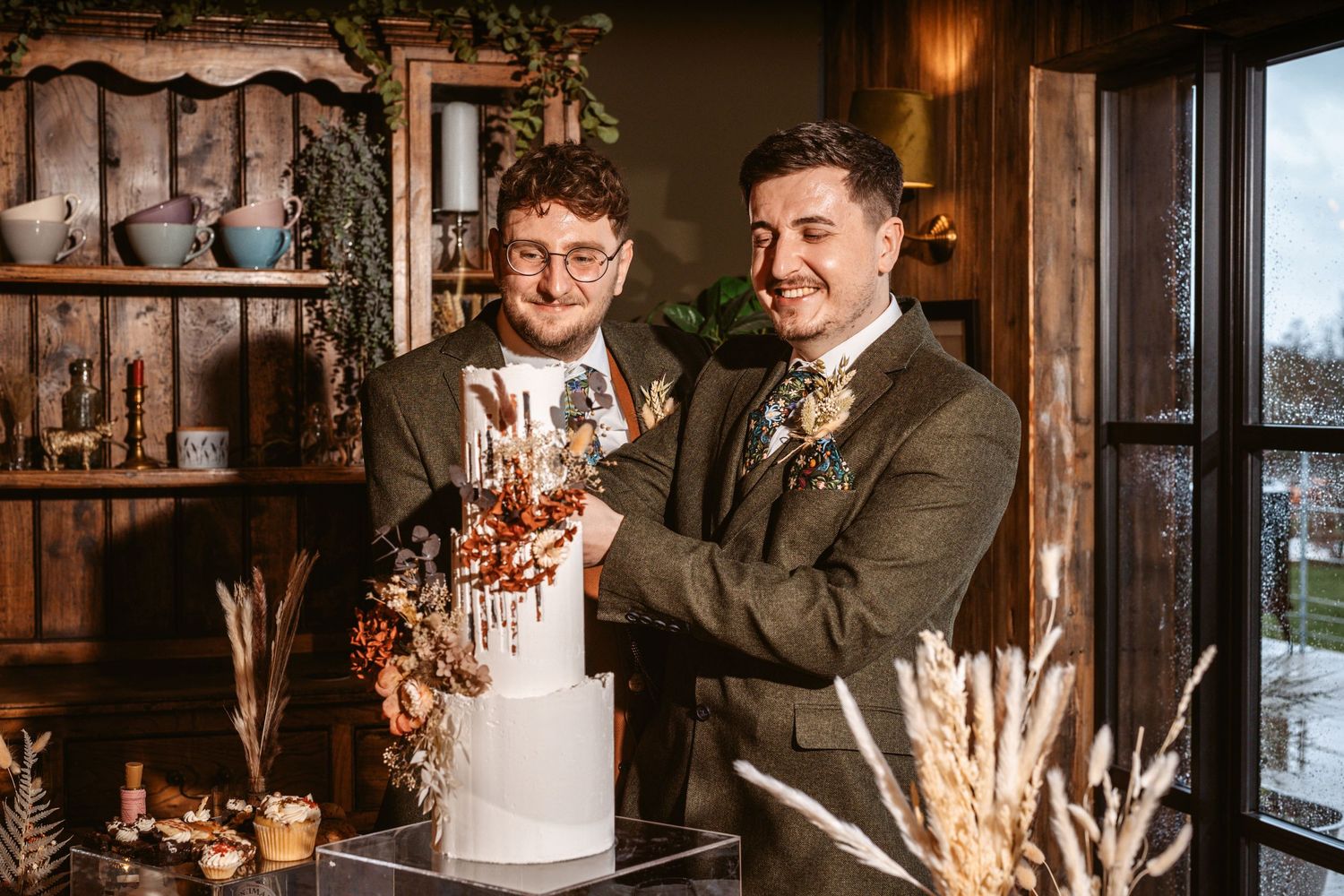 Two people cutting an elegant white wedding cake together in a rustic indoor setting.