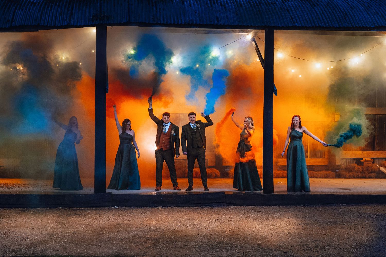 Wedding party poses in silhouette against dramatic orange and blue smoke backdrop.