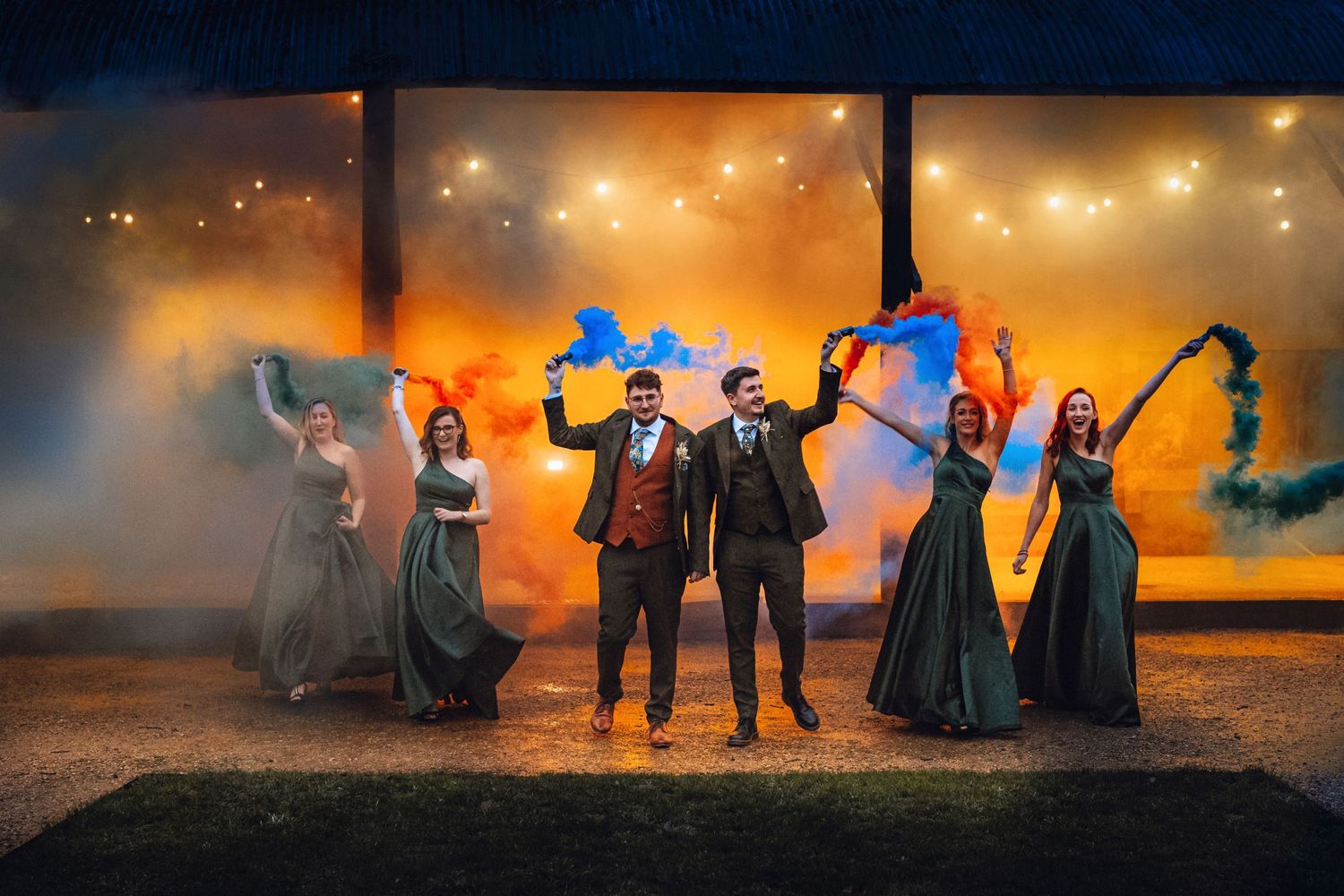 Dramatic wedding photo with smoke effects and blue lighting against orange sunset backdrop.