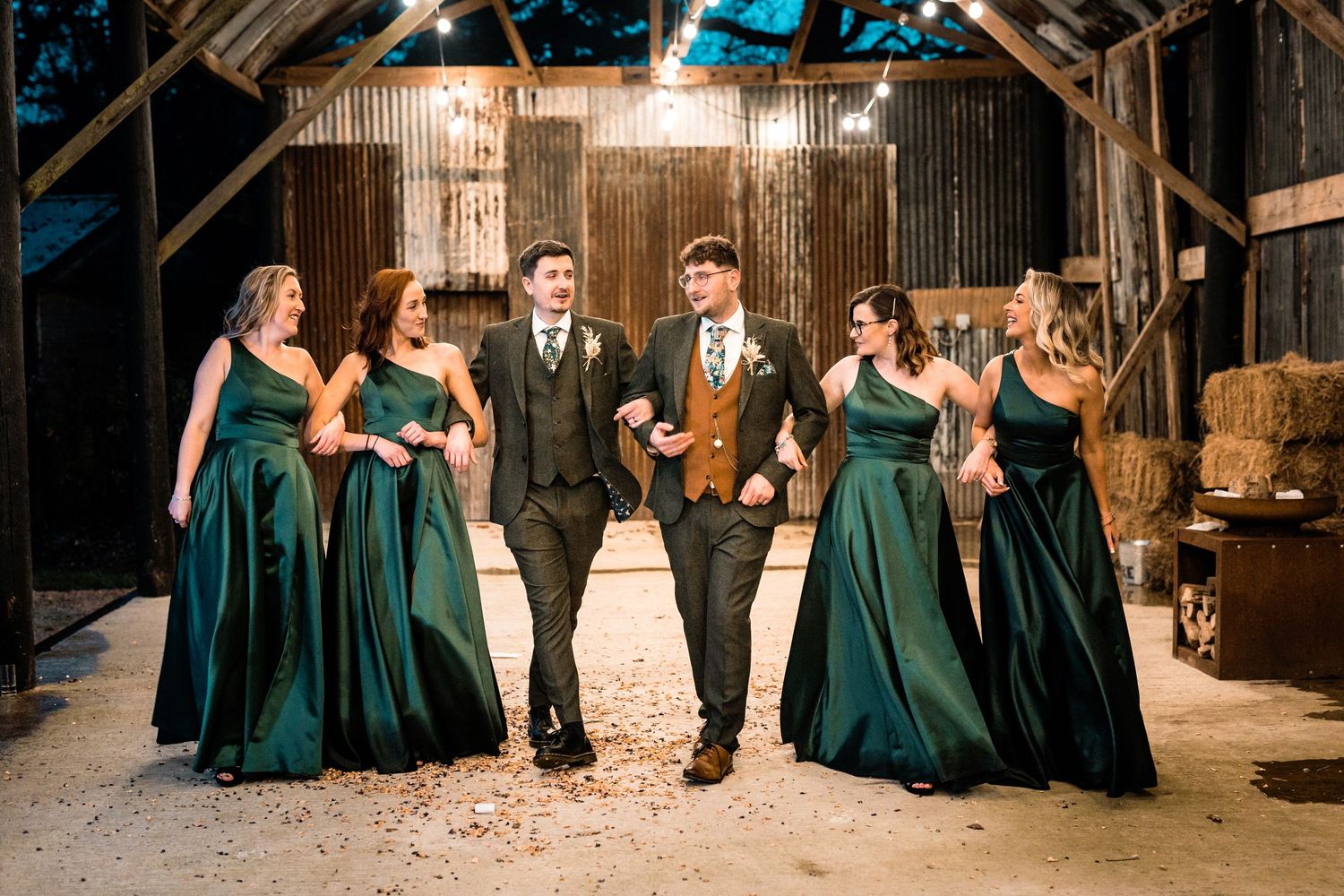 Wedding party in emerald green dresses celebrates in rustic barn setting.