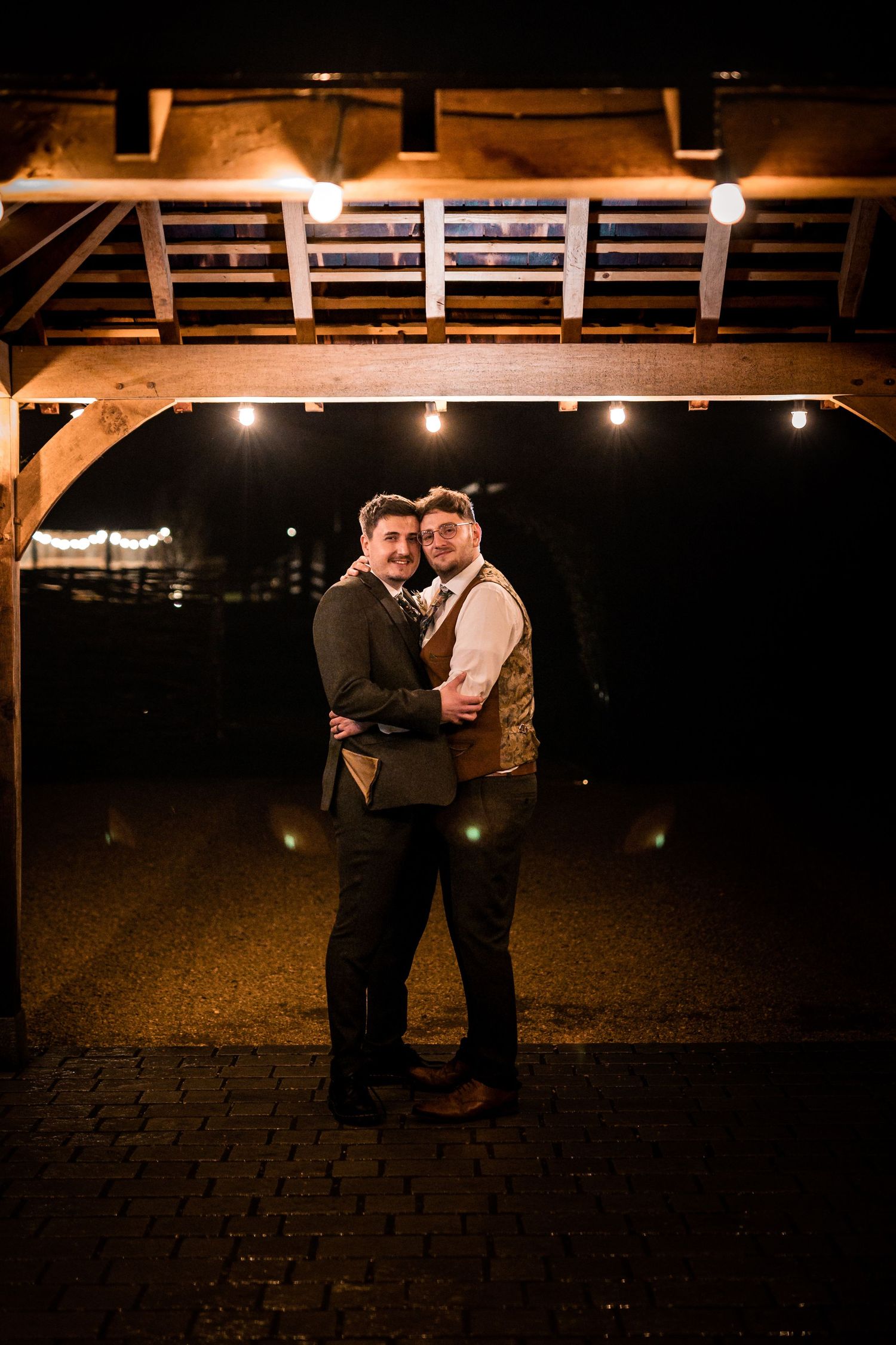 Romantic nighttime portrait under wooden pavilion with warm lighting.