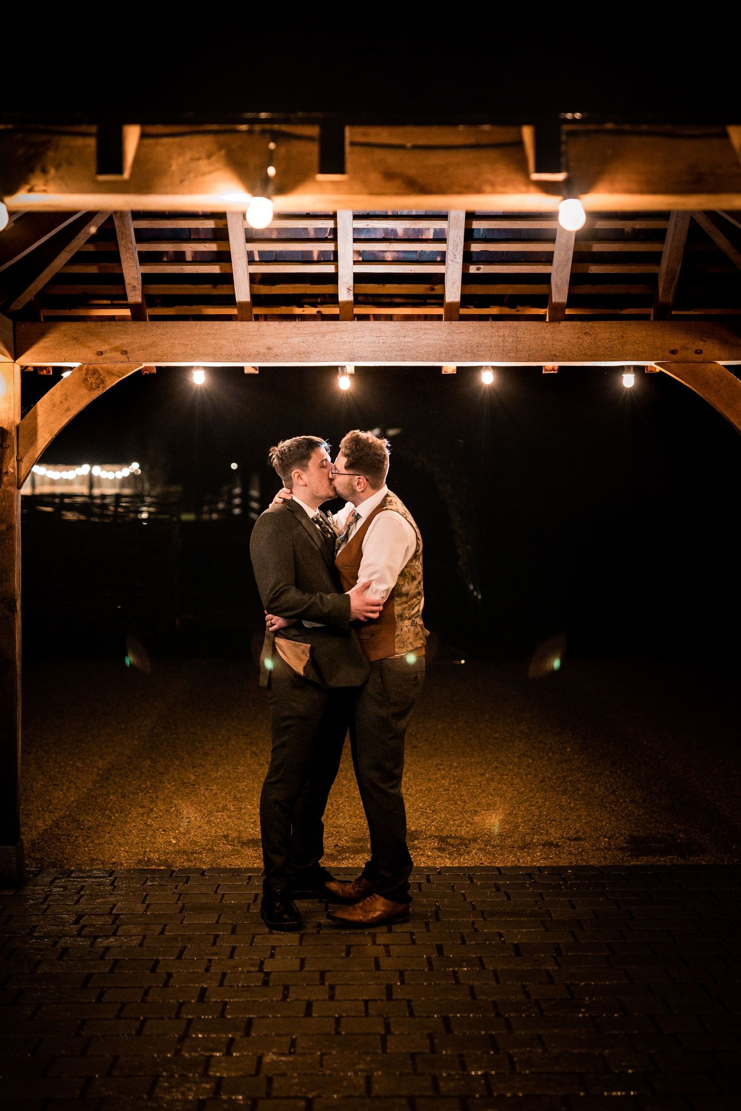 A tender embrace under wooden beams illuminated by soft overhead lighting at night.