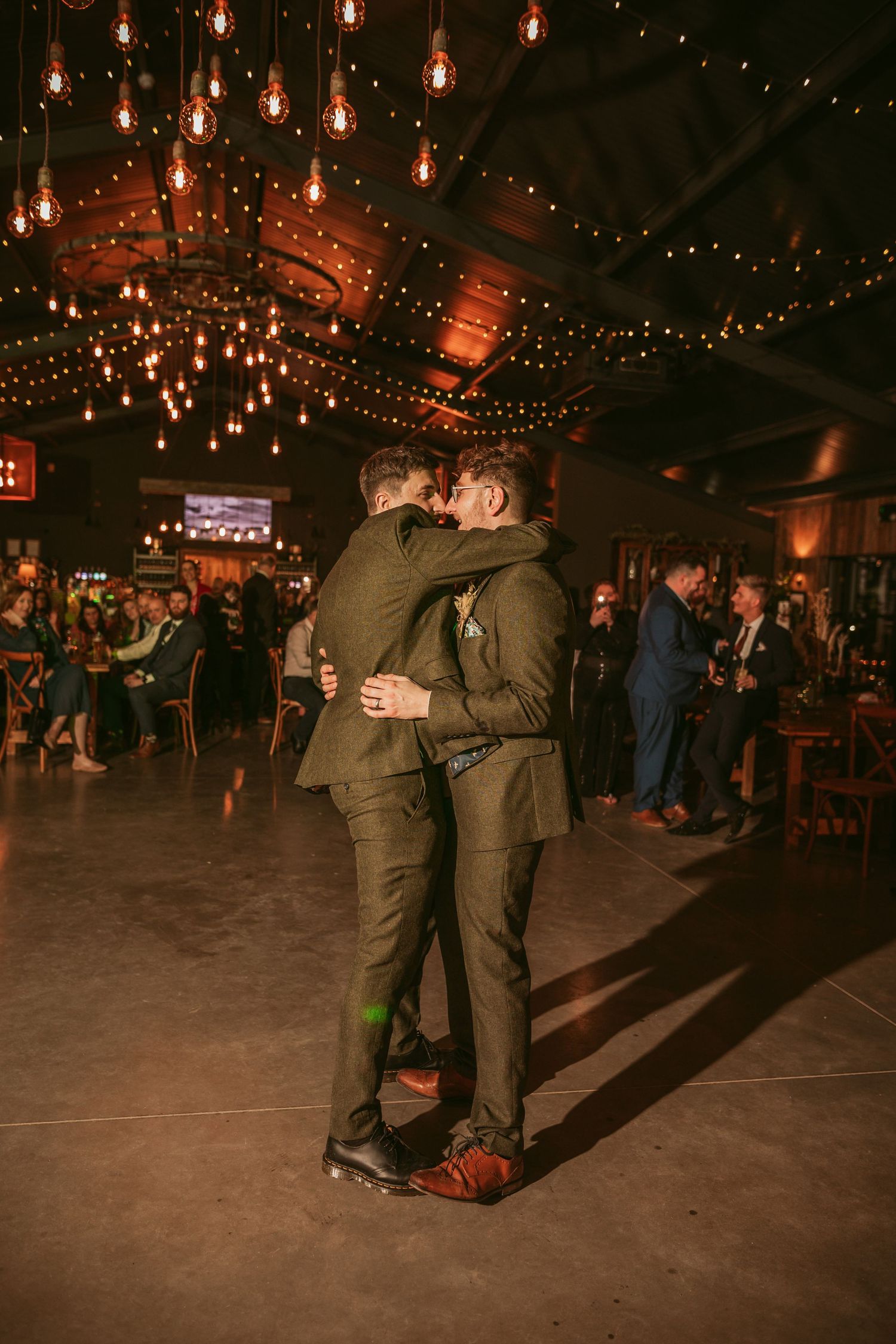 A romantic dance under warm Edison bulbs in a rustic venue with dark ambiance.