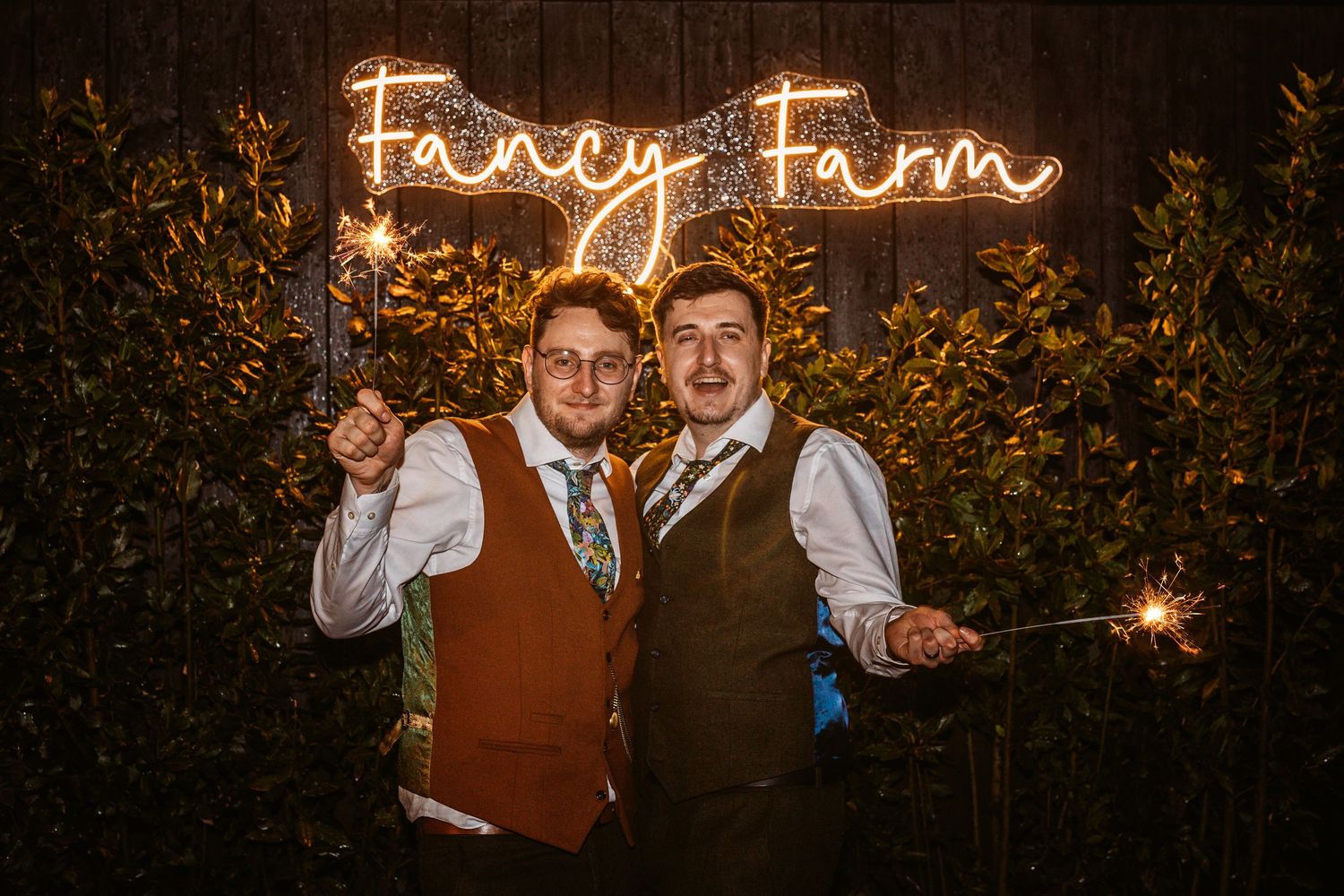 Celebratory pose under illuminated 'Foley Farm' sign with sparklers at night.