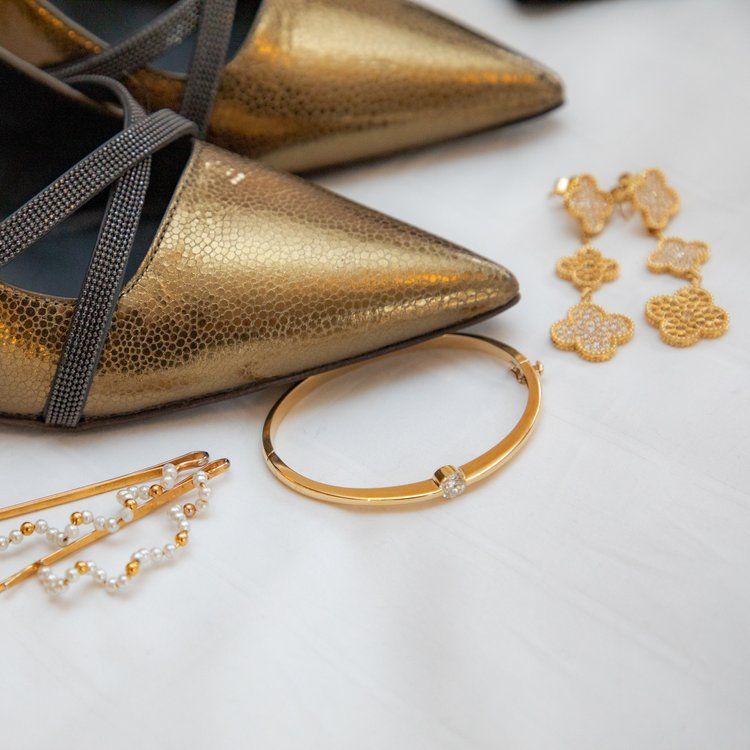 Gold metallic pointed shoes with matching jewelry accessories displayed on white surface.