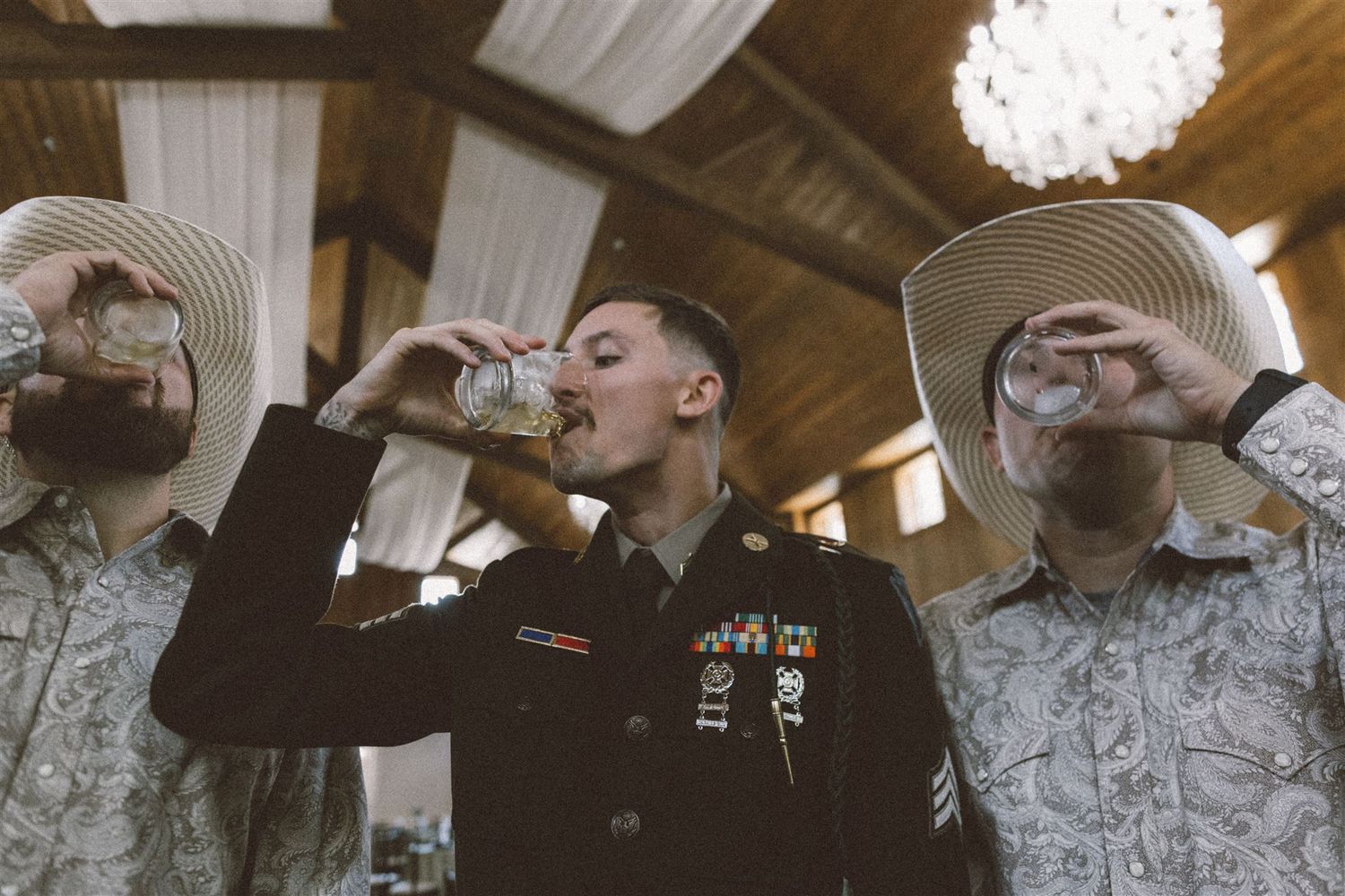 Military members in formal attire and cowboy hats taking shots at a reception.
