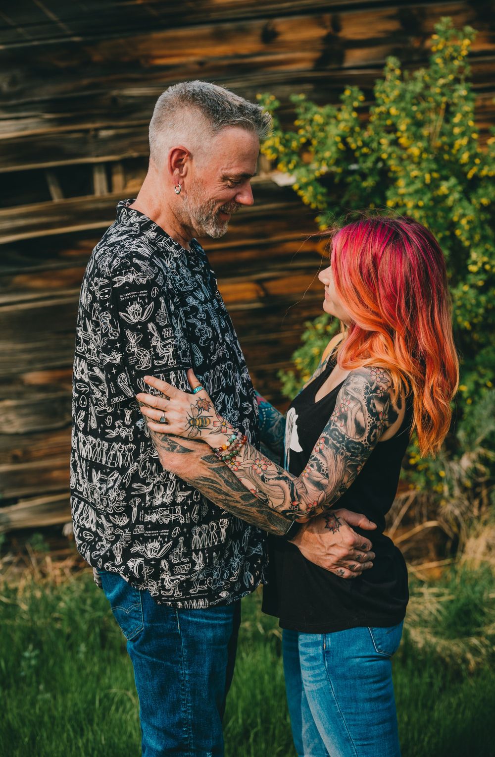 A tattooed couple in casual attire sharing a tender moment outdoors.