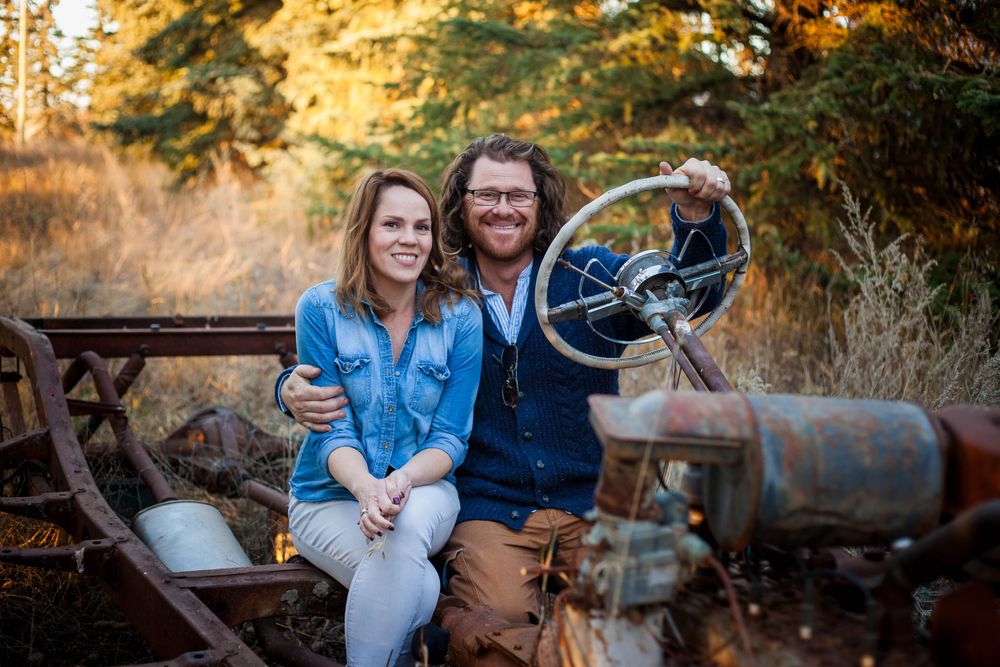 A couple sits together in a rustic outdoor setting with autumn foliage in warm golden light.