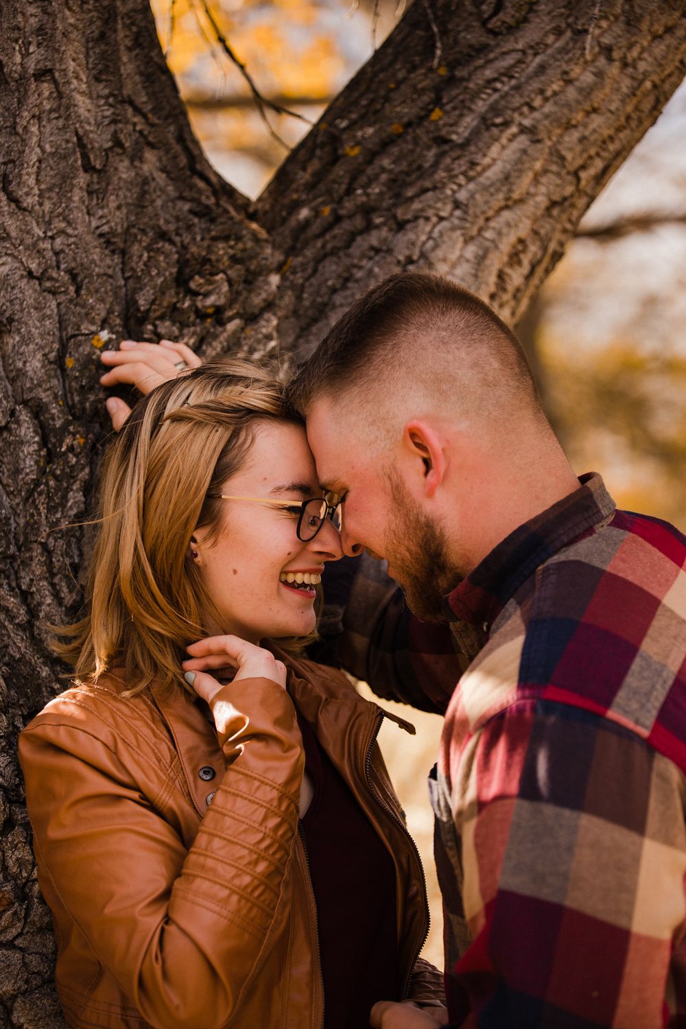 Romantic autumn moment captured between couple sharing intimate laughter by tree.
