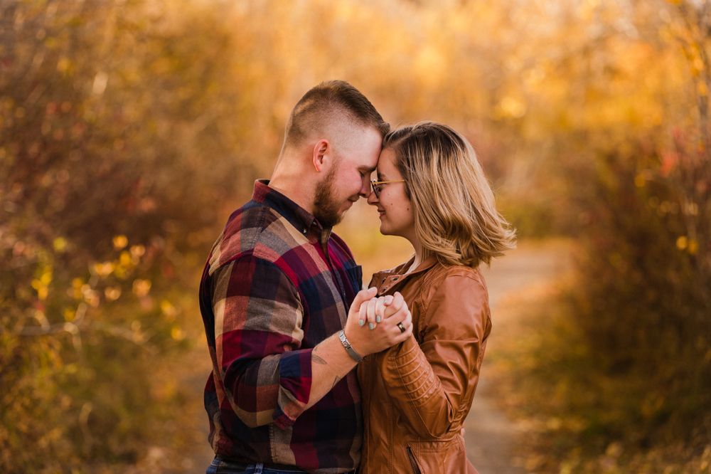 Romantic couple embracing in golden autumn setting with warm fall colors in background.