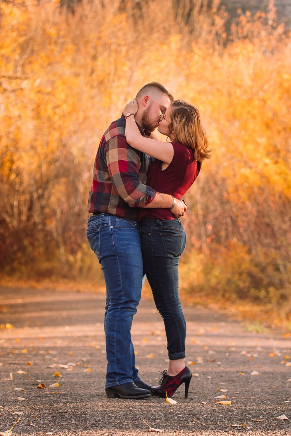 Romantic embrace on autumn path with couple in coordinating red and plaid outfits.