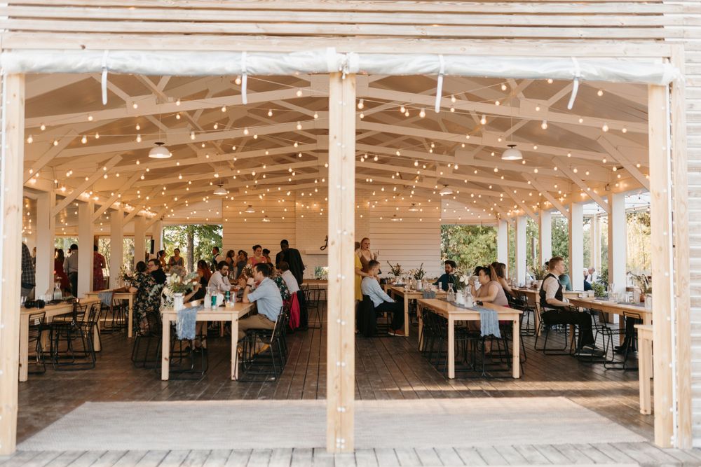 Wedding reception under open-air wooden pavilion adorned with warm string lights and long tables.