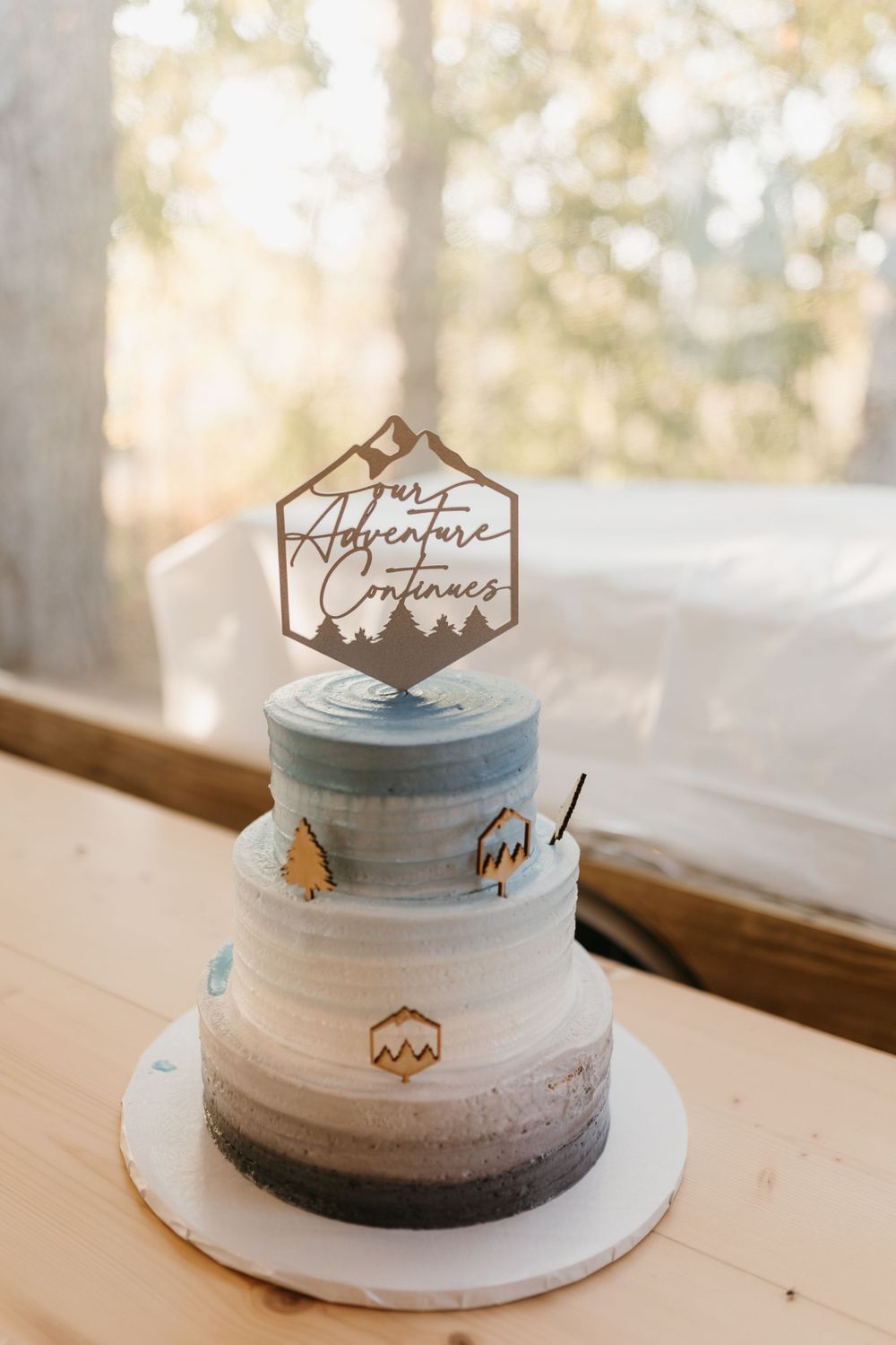 Three-tier ombre wedding cake with mountain adventure topper and wooden decorative accents.