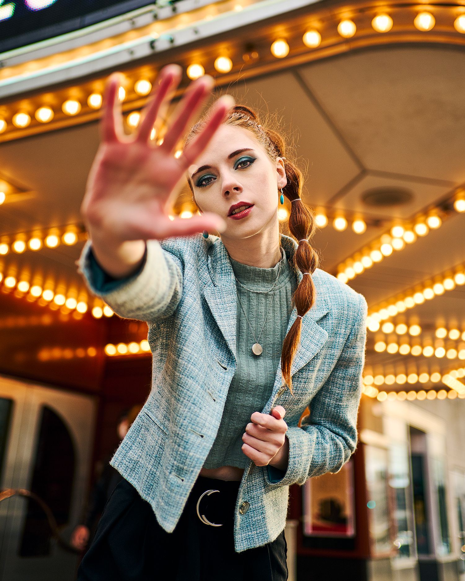 Woman in blue blazer poses dramatically with hand gesture in front of carnival lights at night.