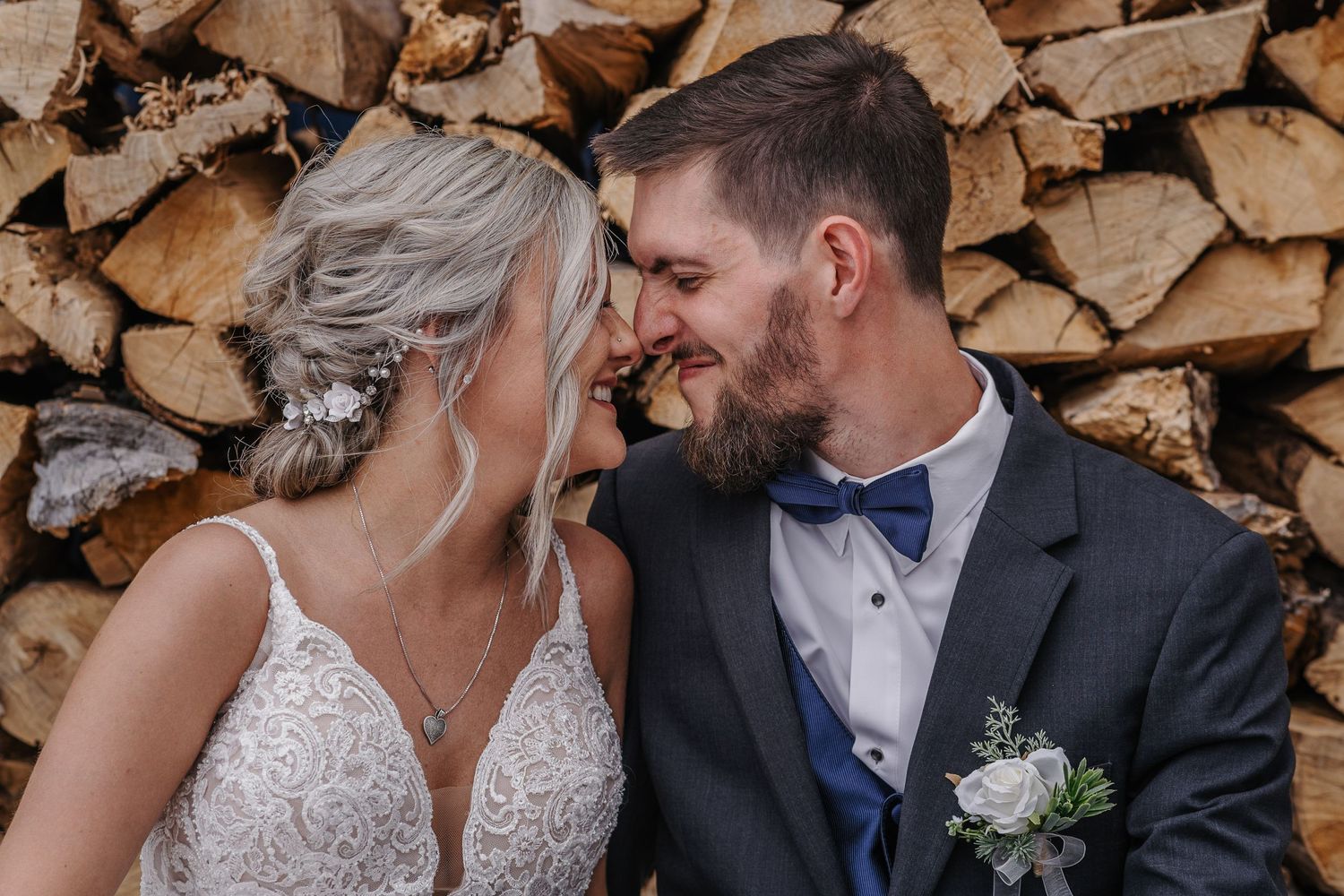 A romantic wedding portrait of a couple sharing a tender moment against a woodpile backdrop.