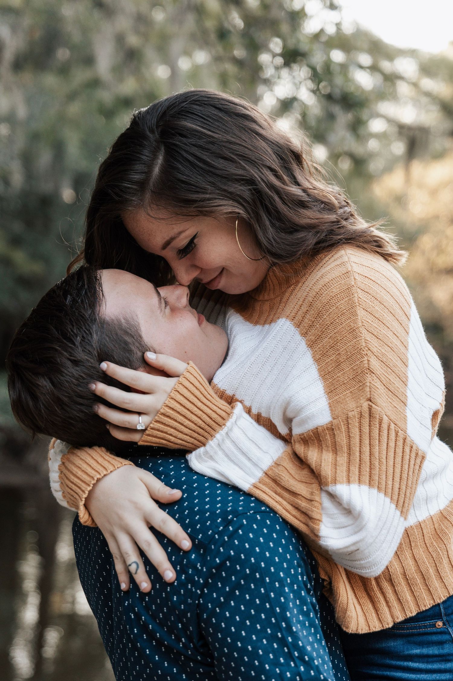 Romantic couple embraces outdoors wearing tan sweater and blue polka dot top in autumn setting.