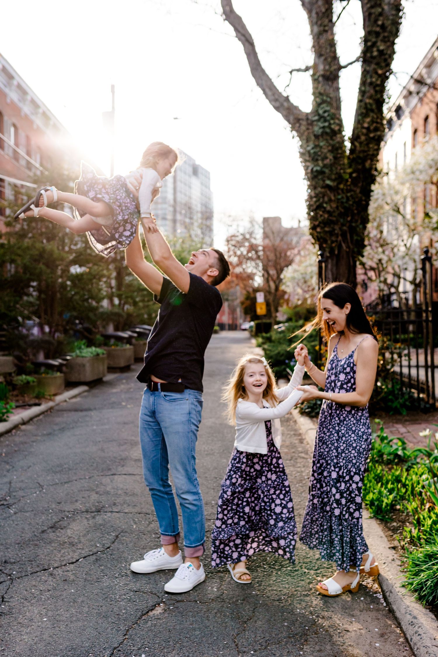 Family enjoying playful moments together on a tree-lined street.