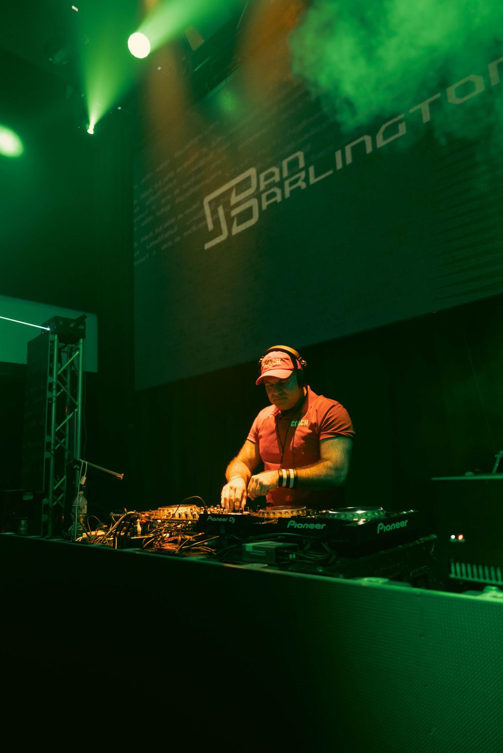 DJ performing at a club with green lighting and professional equipment setup.