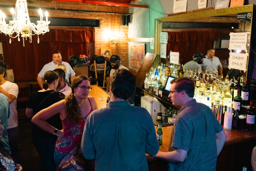 Wide view of a bar interior showing patrons at counter with bottles and glassware visible.
