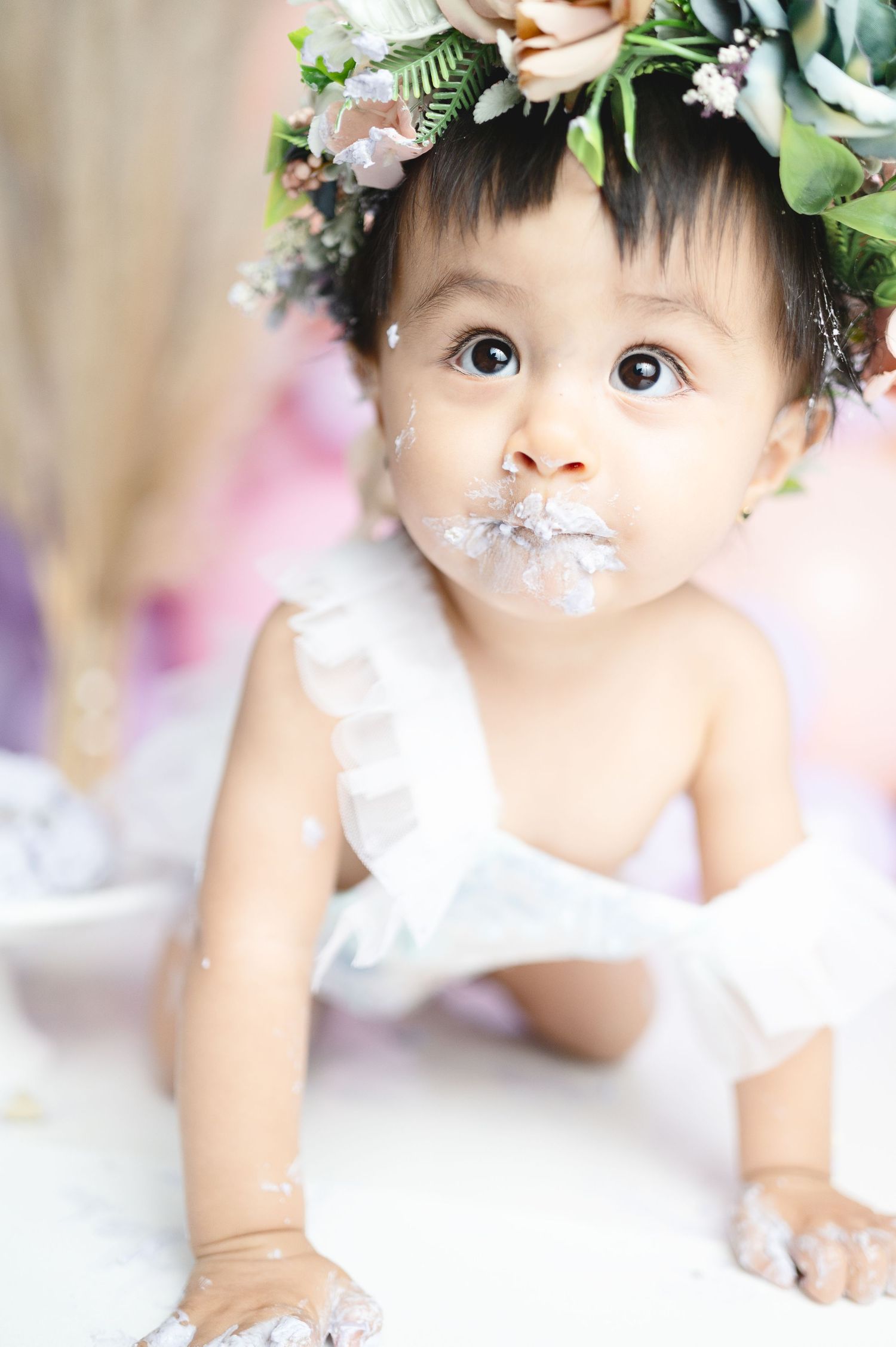 Sweet first birthday celebration setup with floral decorations and white outfit against soft background.