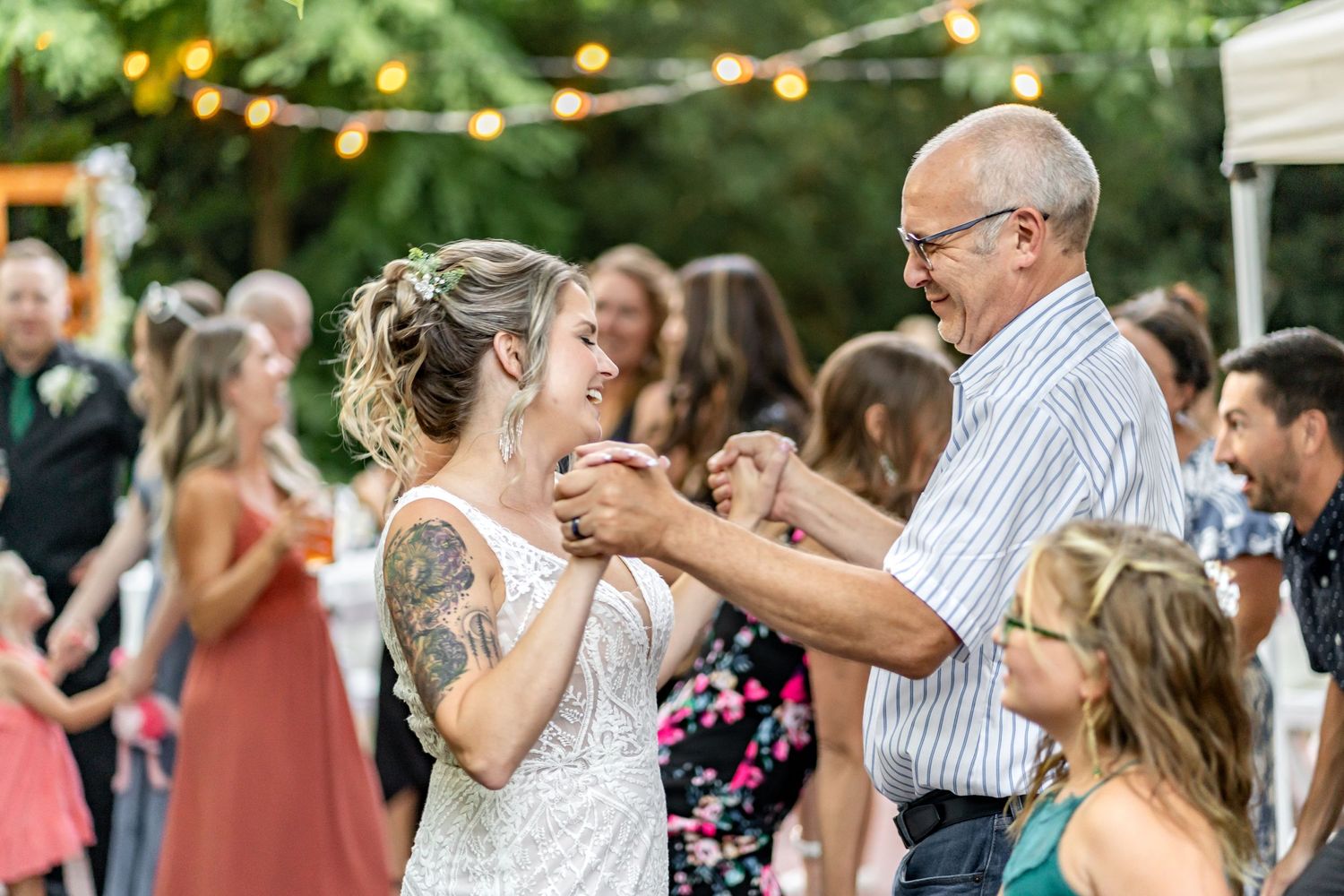 A heartwarming dance moment during an outdoor wedding reception with string lights.