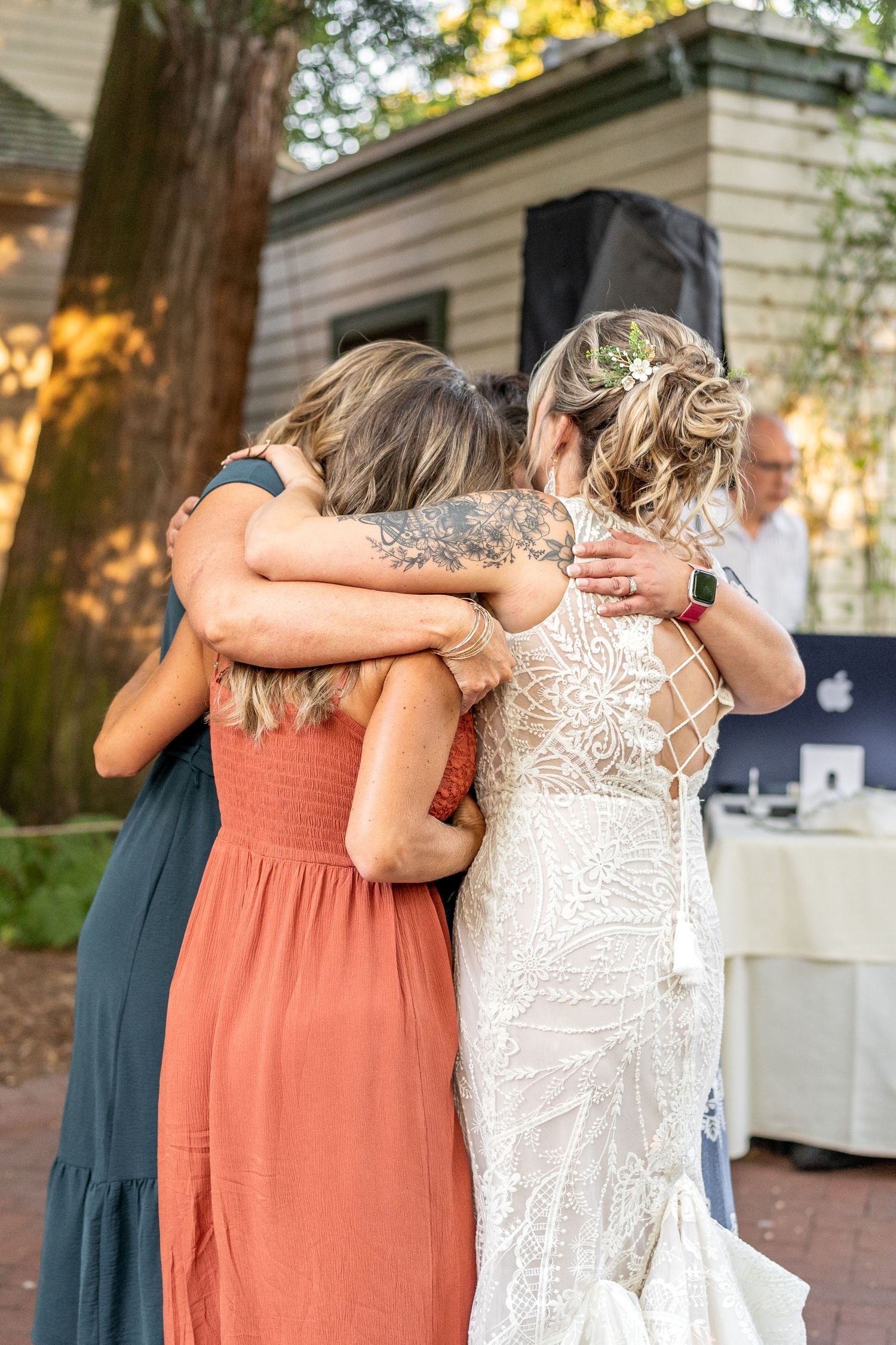 Friends share an emotional group hug at an outdoor wedding reception.