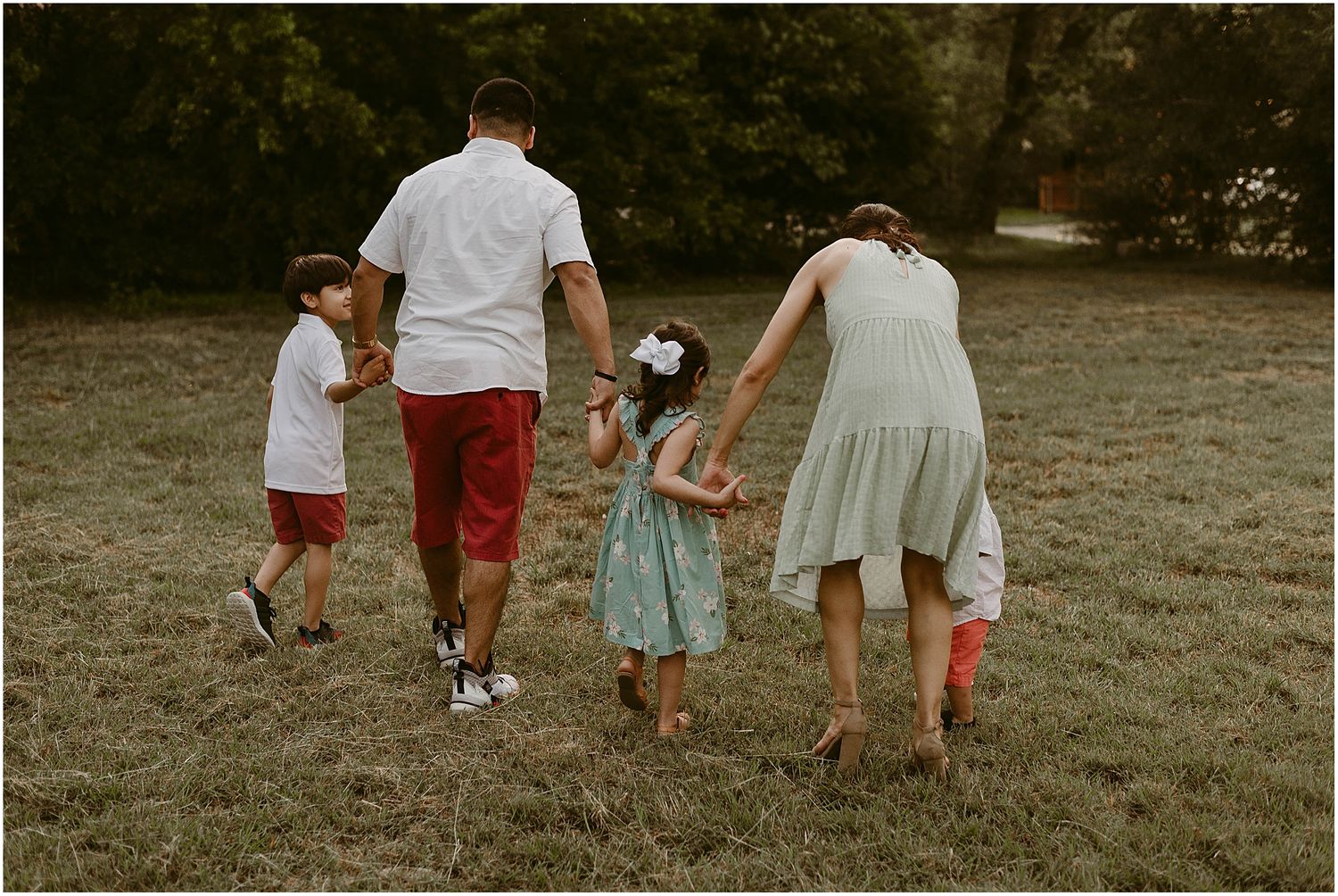 A family walks together hand in hand across a grassy field during golden hour.