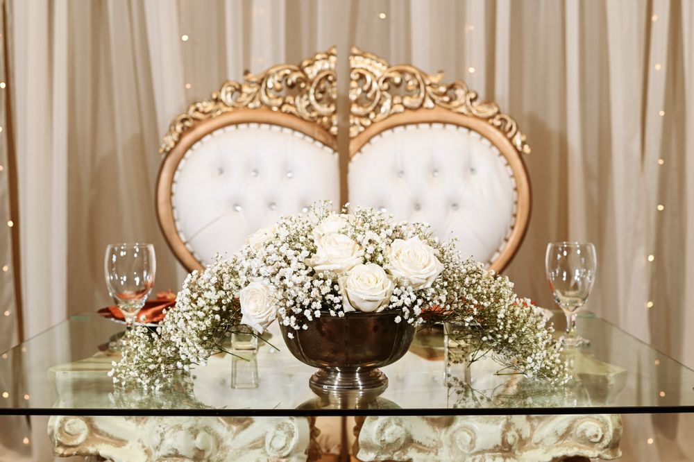 Elegant wedding table setting with ornate gold frame and white floral centerpiece with baby's breath on glass surface.