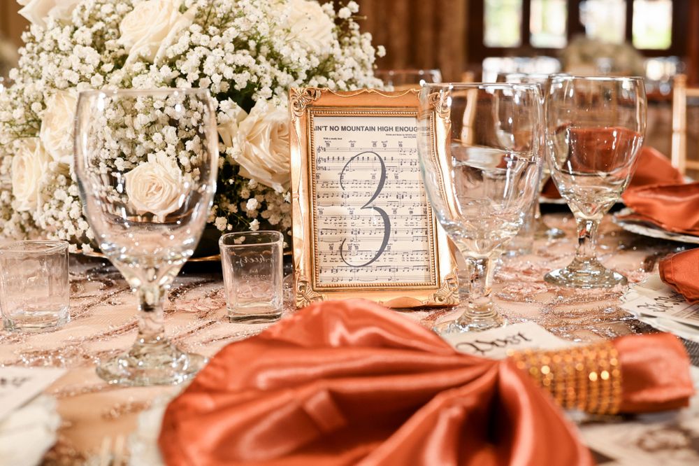 Close up of wedding table decor with coral napkins, crystal glassware and table number in gold frame.