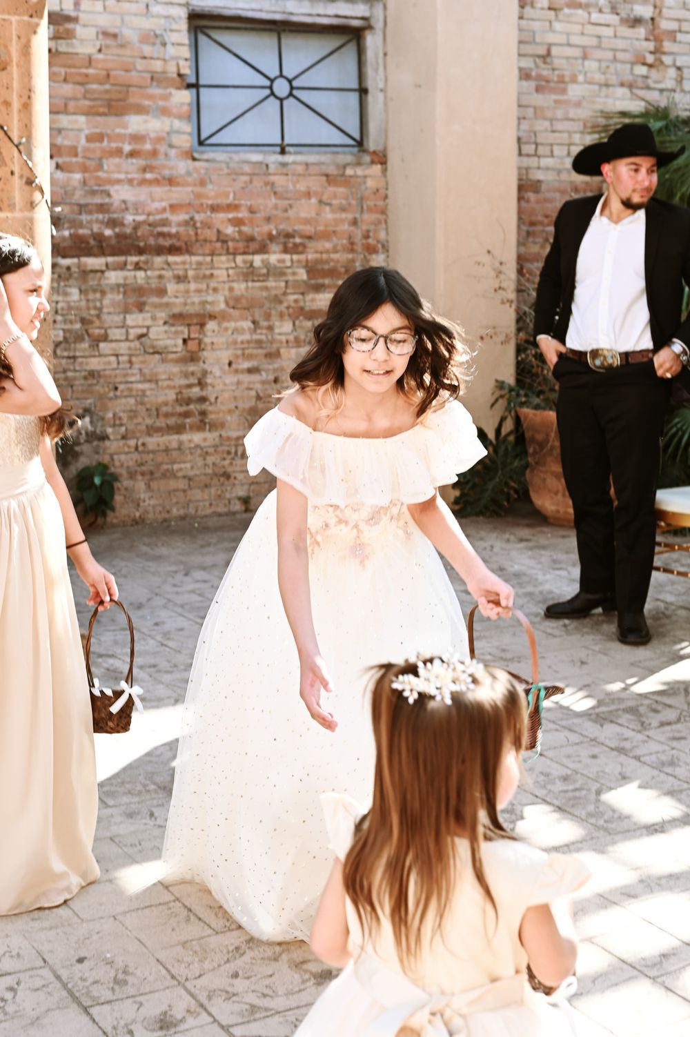 Wedding party members in cream dresses and formal attire gathered in front of brick wall.