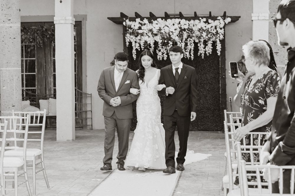 Wedding ceremony processional with attendants walking down an aisle under hanging floral decorations.