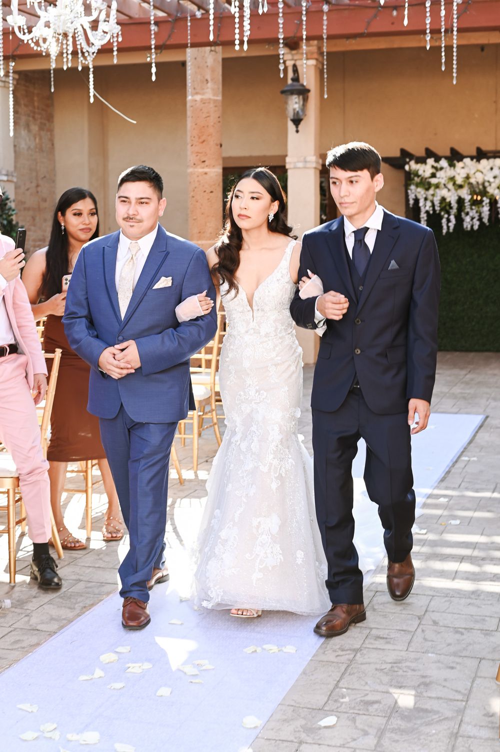 Wedding party members walking down a decorated aisle under hanging crystal decorations.
