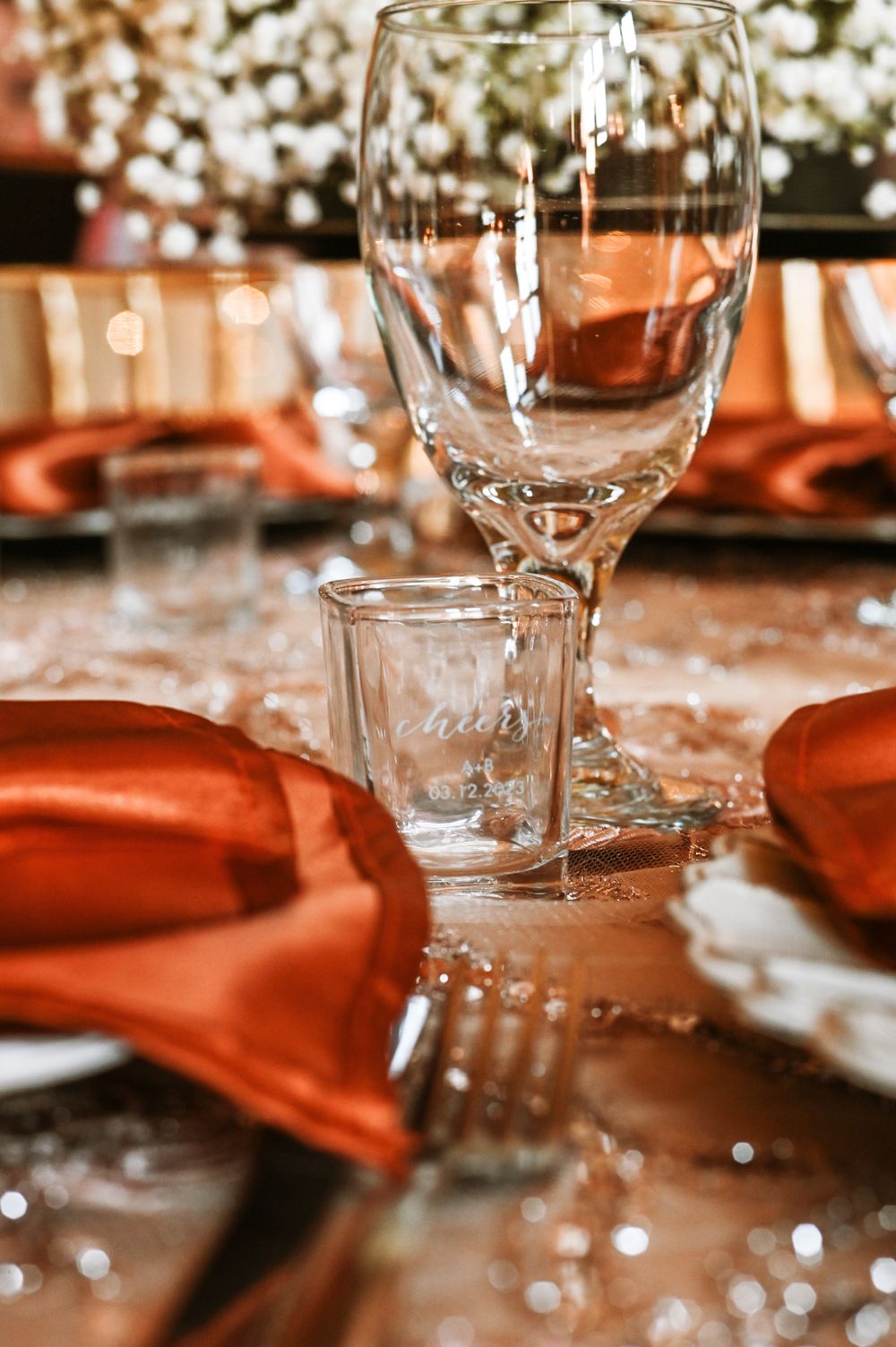 Wedding table setting with empty wine glasses and orange napkins in warm lighting.