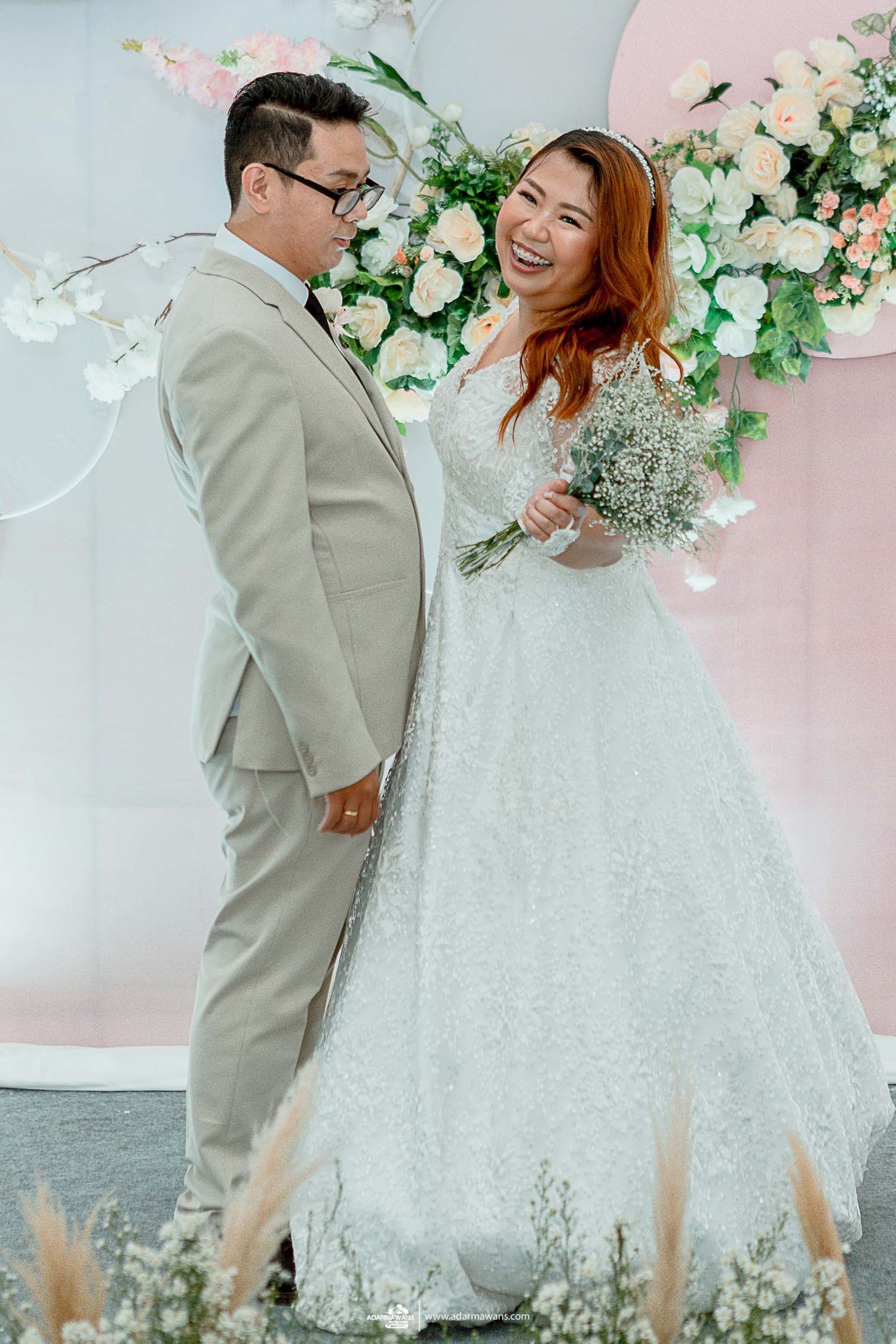 Candid wedding moment captured against pink and white floral backdrop.