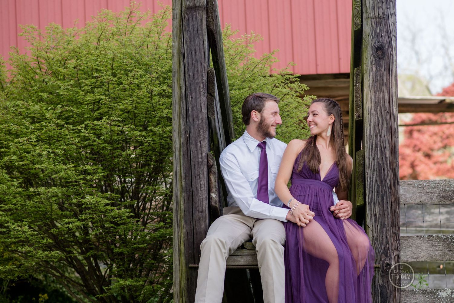 A romantic moment shared between wooden posts against a pink barn backdrop.